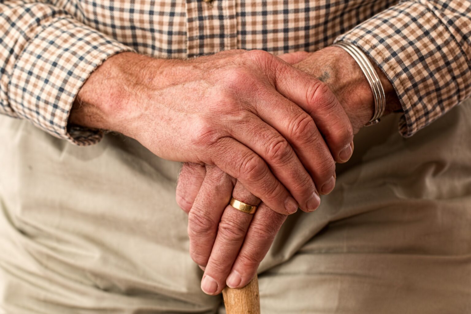 Una persona mayor con sus manos sobre un bastón